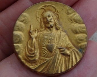 May include: A gold-colored metal religious medal with a depiction of Jesus Christ with a heart on his chest.