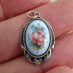 May include: A silver pendant with a white oval cameo featuring a hand-painted pink rose with green leaves and blue flowers.