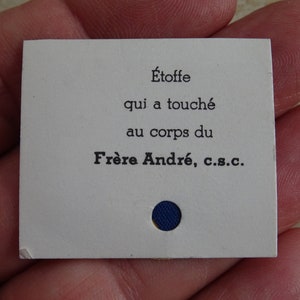 Puede incluir: Una tarjeta blanca con texto negro que dice "Etoffe qui a touché au corps du Frère André, c.s.c.". Un pequeño círculo azul está en el centro inferior de la tarjeta.