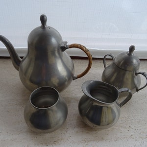 May include: A pewter tea set with a teapot, creamer, sugar bowl, and two cups. The teapot has a brown wicker handle. The set is in a pear shape.