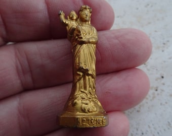 May include: Gold-colored metal figurine of the Virgin Mary holding a baby Jesus. The figurine is standing on a base with the word "FRANCE" inscribed on it.