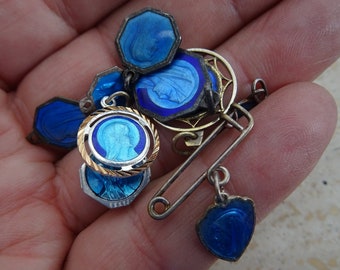 May include: A vintage blue enamel pin with a safety pin closure. The pin features multiple charms with images of the Virgin Mary. The charms are connected by a chain and have a gold-tone finish.