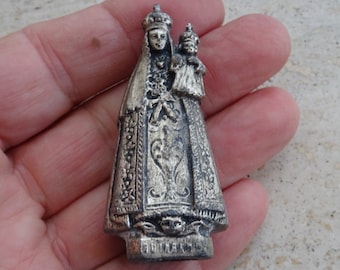 May include: Silver-toned metal figurine of the Virgin Mary holding a baby Jesus. The figurine is detailed with intricate designs and the inscription "Fatima" at the base.