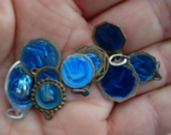 May include: A collection of small, blue and white enamel charms with silver-toned metal accents. The charms are round and feature various designs, including a hand, a flower, and a geometric pattern.