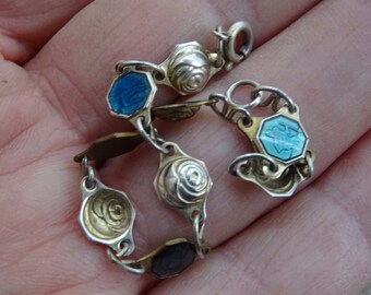 Puede incluir: Una pulsera de plata vintage con eslabones ornamentados. La pulsera presenta elementos decorativos alternos, incluyendo octágonos esmaltados en azul y negro, y detallados eslabones plateados en forma de rosa. Es una joya delicada.