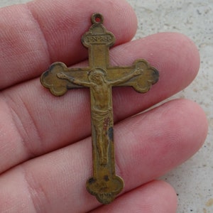 May include: A small, antique, brass crucifix with a depiction of Jesus Christ on the cross. The inscription "I.N.R.I." is visible above the figure.