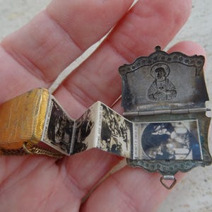 Pode incluir: Um medalhão religioso vintage com uma caixa retangular dourada e uma moldura articulada prateada. O medalhão abre para revelar uma série de pequenas imagens a preto e branco e um ícone religioso.
