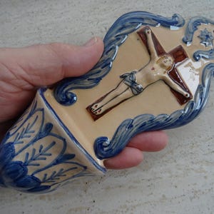 Könnte beinhalten: Eine blaue und weiße Keramik-Wandplakette mit einer Darstellung von Jesus am Kreuz. Die Plakette hat ein kleines, dekoratives Regal unten.