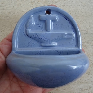 Könnte beinhalten: Ein hellblauer Keramik-Weihwasserbecken mit einem Kreuz und einem stilisierten Öllampe-Design.