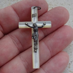 Pode incluir: Um crucifixo de madrepérola branca com uma figura de Jesus prateada. O crucifixo tem um laço no topo para pendurar.