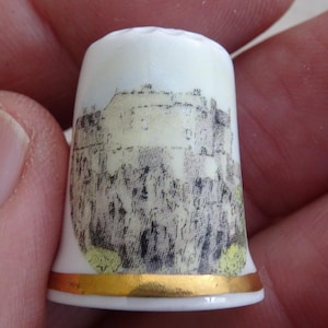 May include: White ceramic thimble with a gold trim and a black and white image of a castle on the front.