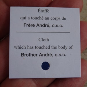 Puede incluir: Tarjeta blanca con texto azul que dice "Étoffe qui a touché au corps du Frère André, c.s.c. Cloth which has touched the body of Brother André, c.s.c."
