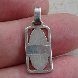 May include: Silver pendant with an oval cutout and a decorative border. The pendant has a loop at the top for attaching to a chain.