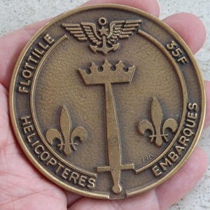 May include: A bronze coin with the inscription "Flotille Helicopters Embarques 35F" and a stylised image of a sword, crown, and fleur-de-lis.