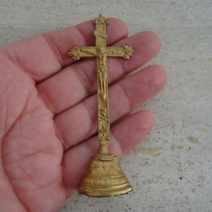 May include: A gold-colored metal crucifix with a figure of Jesus Christ on the cross. The crucifix is on a stand with a bell-shaped base.
