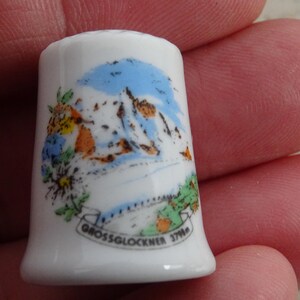 以下が含まれることがあります： 白い磁器製の指ぬきで、カラフルな山脈の画像と「Grossglockner 3798」の文字が描かれています。