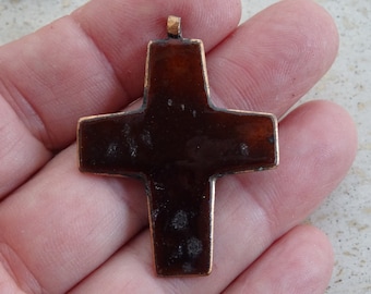 May include: A dark brown metal cross pendant with a loop at the top for hanging. The cross has a smooth, slightly textured surface.