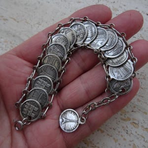 Puede incluir: Pulsera plateada con pequeños dijes redondos con diseños arquitectónicos, unidos por delicadas cadenas. La pulsera tiene un cierre. Estilo vintage, los dijes miden aproximadamente 1,5 cm de diámetro.