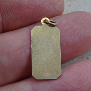 May include: Gold-toned metal charm with a rectangular shape and rounded corners. The charm has a smooth surface and the inscription "FOREVER 1220 14K GR" on the bottom.