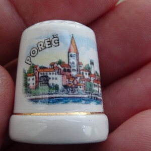Könnte beinhalten: Weiße Keramik-Fingerhut mit einer bunten Illustration einer Stadt mit einem hohen Turm und dem Wort "POREČ" auf der Seite.