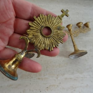 May include: Two gold-toned metal religious candle holders. One holder has a circular design with a cross on top. The other holder has three candle cups.