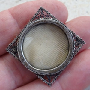 May include: A silver locket with a filigree design and a round glass window. The locket is closed and the glass is clear.