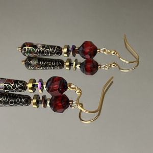 May include: A pair of dangle earrings with black and gold enamel beads, red faceted glass beads, and gold-toned hooks.
