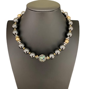 Może przedstawiać: Czarny i złoty naszyjnik z koralików z dużą, okrągłą, wielokolorową koralikiem mozaikowym w środku.