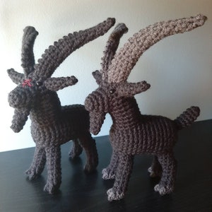 May include: Two crocheted brown goats with long horns. The goats are standing on a dark surface.