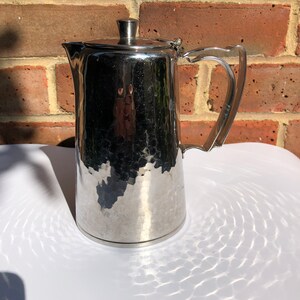 Puede incluir: Una cafetera de acero inoxidable martillado plateado con tapa y asa.