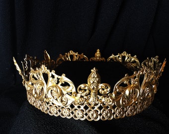 Puede incluir: Una corona dorada con intrincados diseños florales y de volutas. La base circular de la corona está adornada con elementos decorativos y acentos puntiagudos. El diseño ornamentado y el acabado metálico le dan una apariencia regia.