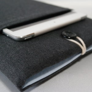 May include: A gray fabric tablet sleeve with a button closure and a white strap. The sleeve has a light blue lining and a tablet is inside.