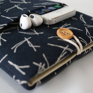 May include: A dark blue fabric phone case with a white pattern of lines. The case has a pocket for earbuds and a button closure. A white smartphone and white earbuds are inside the case.