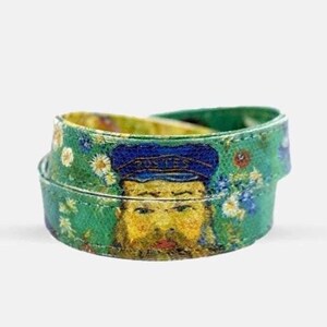 Puede incluir: Un brazalete de tela verde y azul con una imagen impresa de la cara de un hombre con un sombrero azul. La imagen está rodeada de flores amarillas.