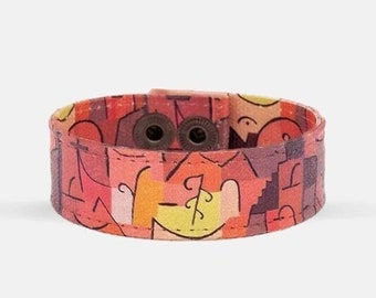 Op de afbeelding: Een kleurrijk stoffen armband met een geometrisch patroon in tinten rood, oranje, geel en bruin. Het armband heeft een gespsluiting met twee metalen drukknopen.