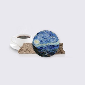 Puede incluir: Un posavasos redondo con una imagen azul y blanca de La noche estrellada de Van Gogh. El posavasos est&aacute; sobre una superficie marr&oacute;n texturizada.