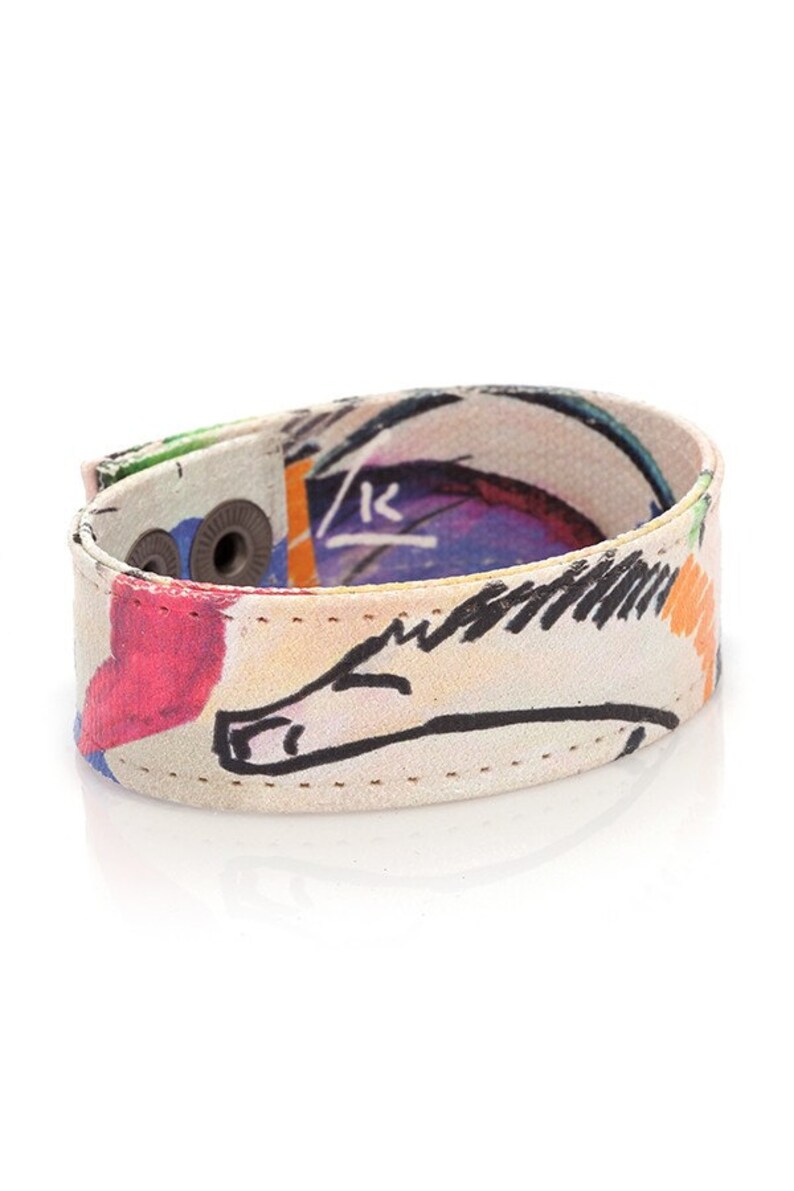 Op de afbeelding: Een kleurrijke canvas armband met een witte achtergrond en een zwart-witte tekening van een paard. De armband heeft twee zilveren drukknopen en is gestikt met wit garen.