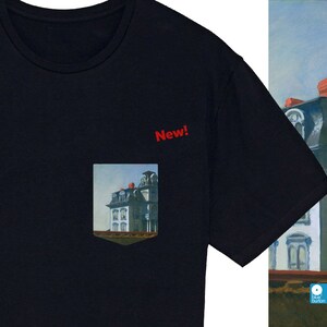 Peut inclure: Un t-shirt noir avec une poche repr&eacute;sentant une peinture d'une maison. La poche porte l'inscription "New!" au-dessus.