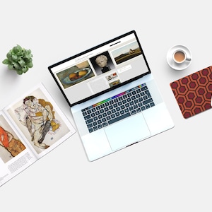 Pu&ograve; includere: Un computer portatile con uno sfondo bianco e un tappetino per mouse con un motivo geometrico. Il laptop &egrave; aperto e mostra un sito web con immagini d'arte. Ci sono due libri con immagini d'arte sul lato sinistro del laptop. Una piccola pianta in vaso si trova nell'angolo in alto a sinistra dell'immagine. Una tazza di caff&egrave; si trova nell'angolo in alto a destra dell'immagine.