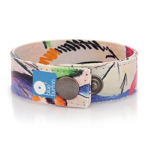 Op de afbeelding: Een kleurrijk stoffen armband met een witte achtergrond en een blauwe knoopsluiting. De knop heeft de tekst "blue button" erop.