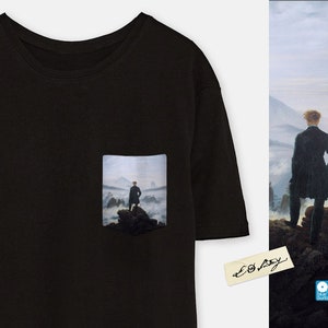 May include: Black t-shirt with a pocket featuring a painting of a man standing on a mountaintop with fog in the background. The painting is titled "Wanderer Above the Sea of Fog" by Caspar David Friedrich.