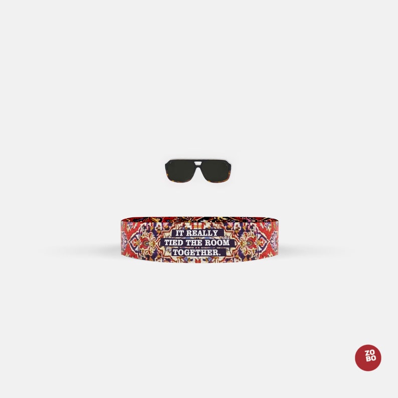 May include: A red, blue, and yellow patterned wristband with the text "It really tied the room together."  The wristband is next to a pair of black sunglasses.