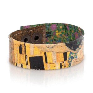 May include: A wide cuff bracelet featuring a print of Gustav Klimt's "The Kiss." The bracelet has a yellow, black, and gold colour scheme with a floral pattern on the inside. It fastens with two metal snaps.