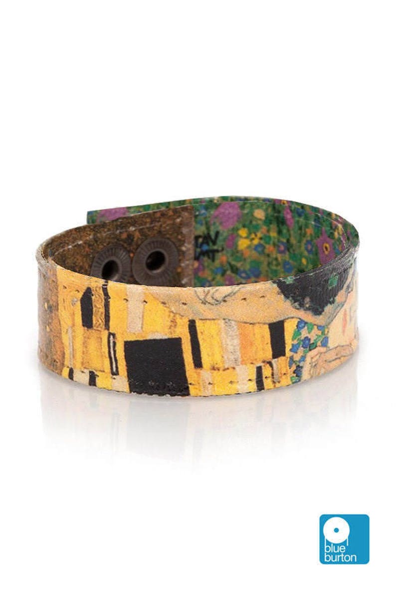 May include: A wide cuff bracelet featuring a print of Gustav Klimt's "The Kiss." The bracelet has a yellow, black, and gold colour scheme with a floral pattern on the inside. It fastens with two metal snaps.
