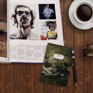 Peut inclure: Un petit carnet noir et vert avec une peinture de sc&egrave;ne de for&ecirc;t sur la couverture. Le carnet porte l'inscription "NOTES" sur le devant. Le carnet est pos&eacute; sur une table en bois &agrave; c&ocirc;t&eacute; d'un stylo, de lunettes de soleil et d'une tasse de caf&eacute;.