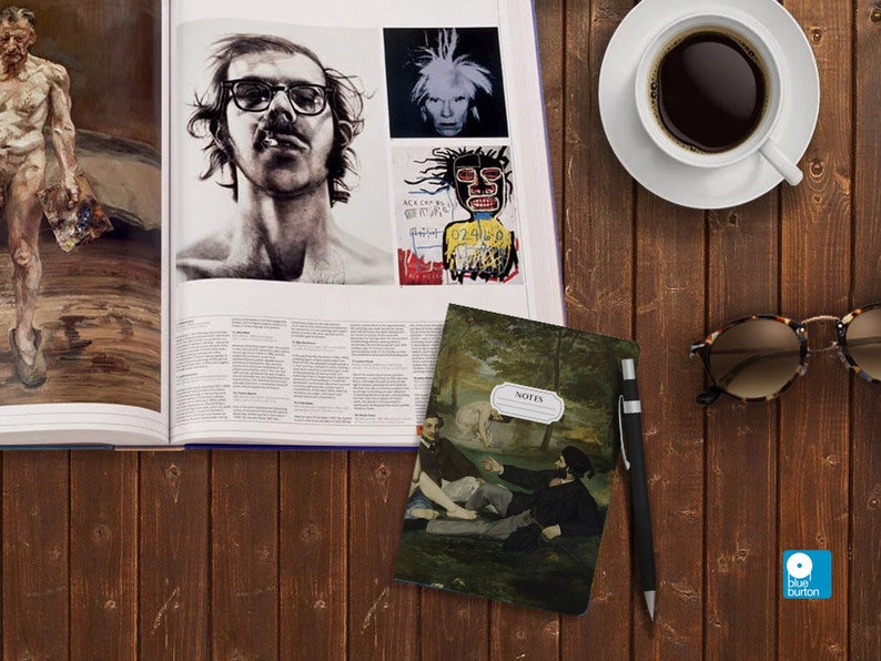 Peut inclure: Un petit carnet noir et vert avec une peinture de sc&egrave;ne de for&ecirc;t sur la couverture. Le carnet porte l'inscription "NOTES" sur le devant. Le carnet est pos&eacute; sur une table en bois &agrave; c&ocirc;t&eacute; d'un stylo, de lunettes de soleil et d'une tasse de caf&eacute;.