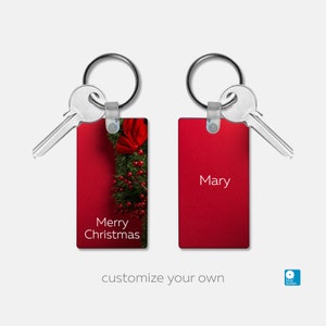 May include: Two red rectangular keychains with silver key rings. One keychain has a Christmas wreath with red berries and the text "Merry Christmas". The other keychain has the name "Mary" in white text.