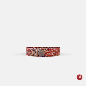 May include: A red, blue, and gold patterned fabric bracelet with a silver metal clasp.