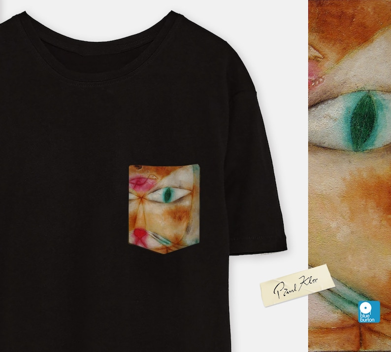 May include: Black t-shirt with a pocket featuring a colourful abstract cat painting by Paul Klee. The pocket is on the left side of the shirt. The painting is in a style reminiscent of cubism.