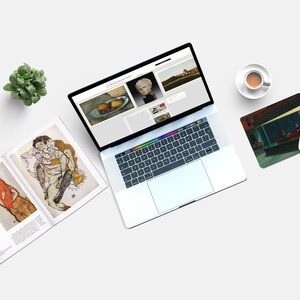 May include: A laptop computer with a white background, a book with two paintings of people, a cup of coffee, and a mouse pad with a painting of a diner scene.